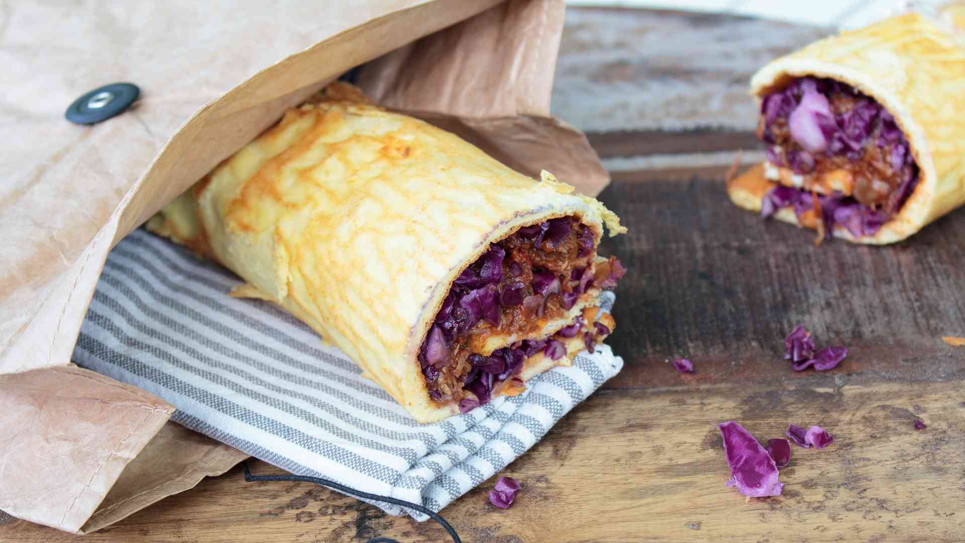 Ein Wrap, gefuellt mit Pulled Chicken liegt auf einem Brett